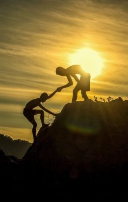 Am image of a man helping another person up a mountain. Success requires help.